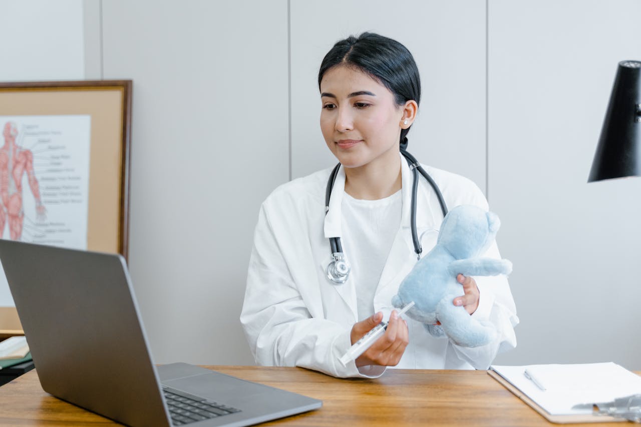 Crafting Captivating Headlines: Your awesome post title goes here Female doctor using a laptop for an online consultation, demonstrating with a syringe and toy.
